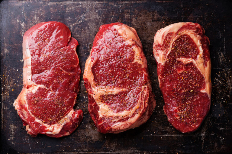 Three cuts of Raw fresh meat Steaks and seasonings on dark background